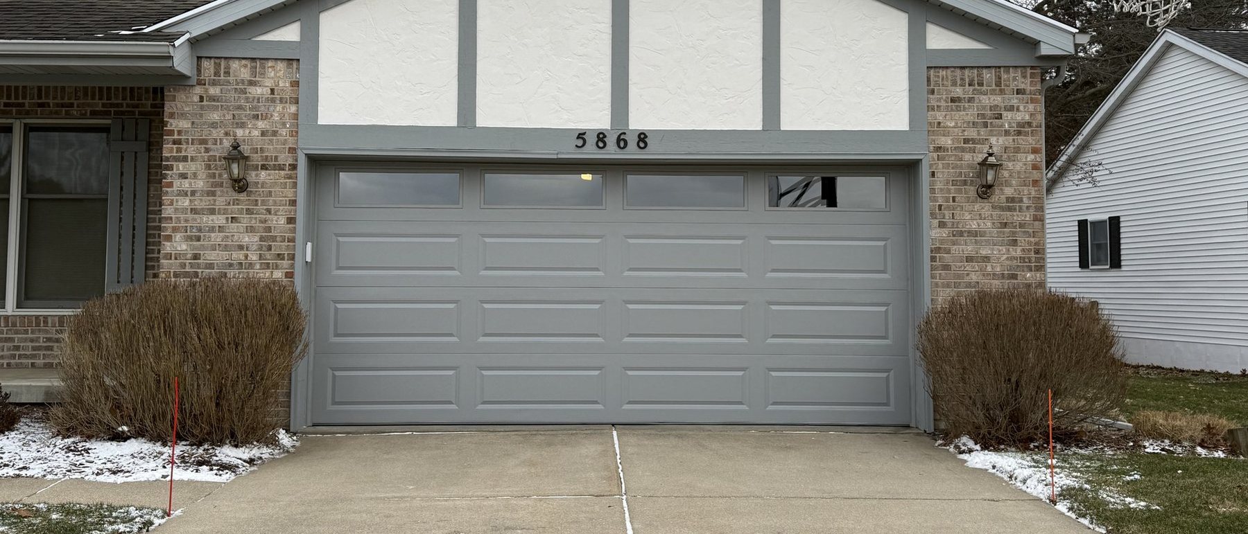 A gray raised-panel garage door on a two-story Lansing-area home in winter