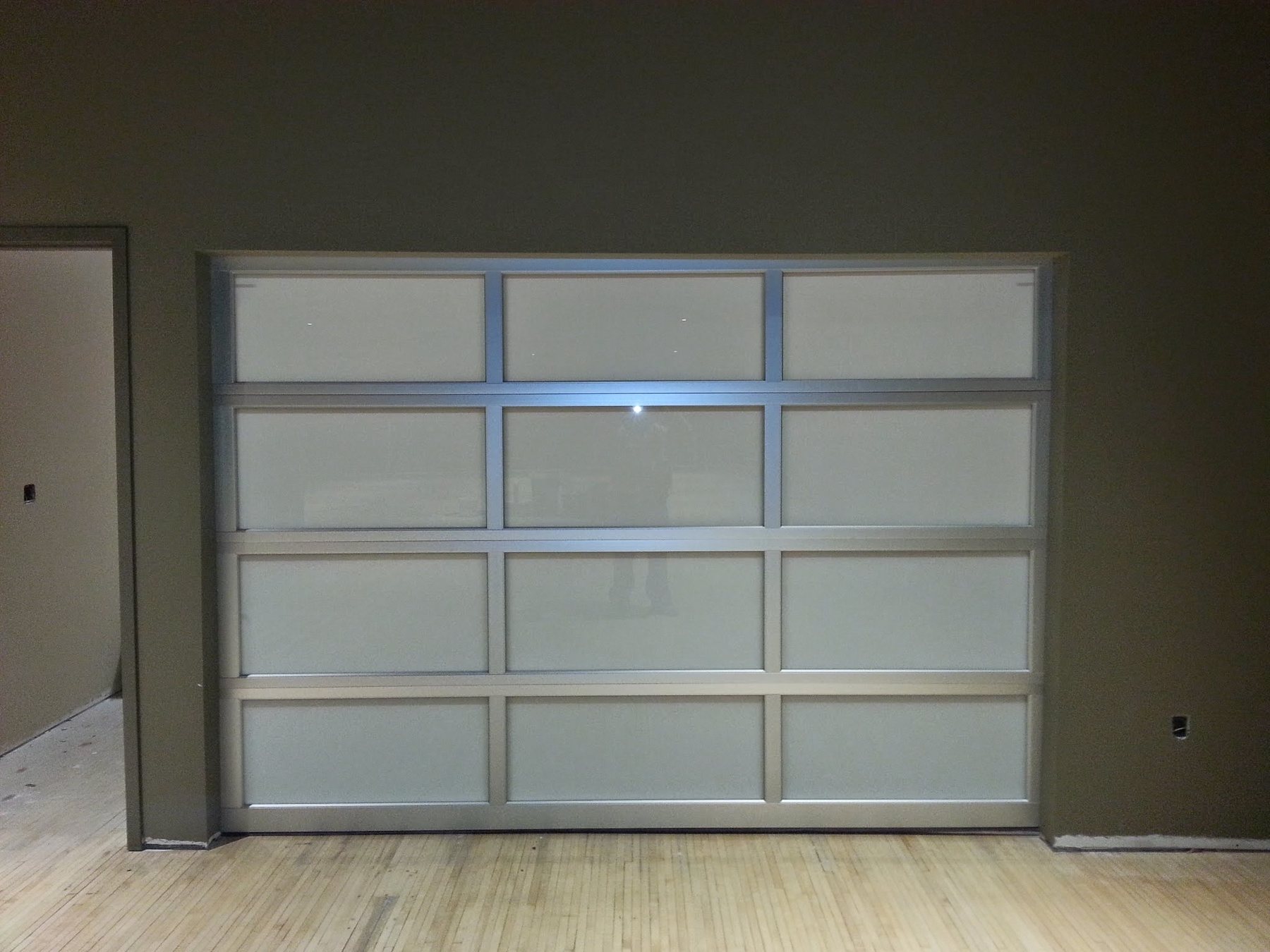 A full-view aluminum garage door with frosted glass panels, seen from inside the garage