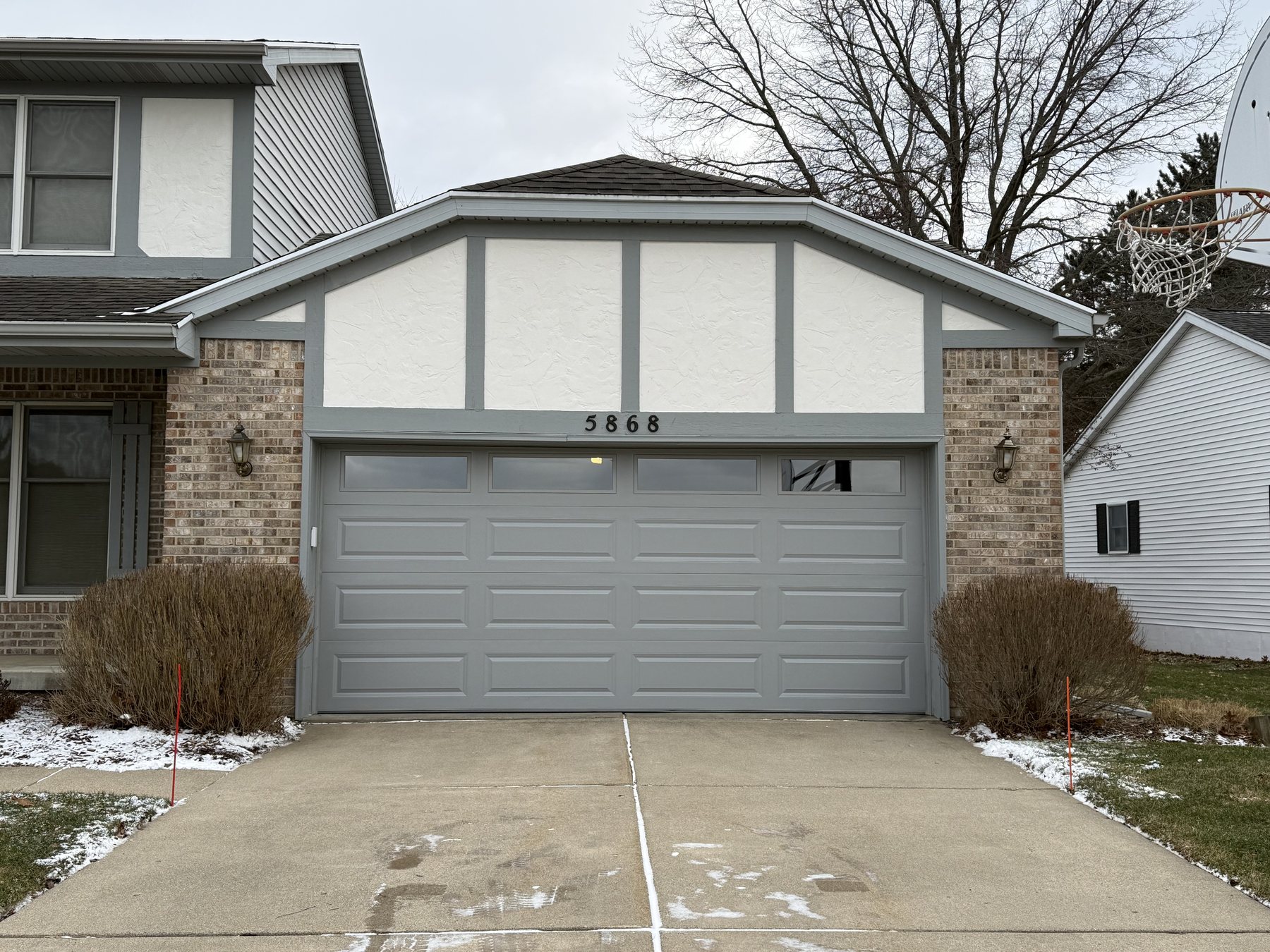 A new light-gray raised-panel garage door on a two-story home in winter, house number 5868 above the opening