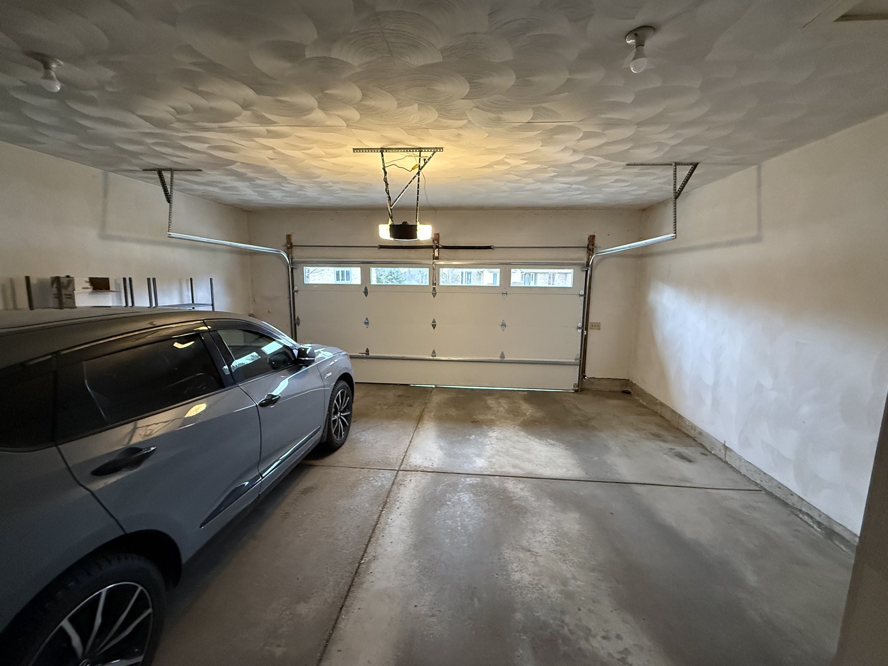 Inside a two-car garage with a car parked, a new opener rail overhead and a white door with windows