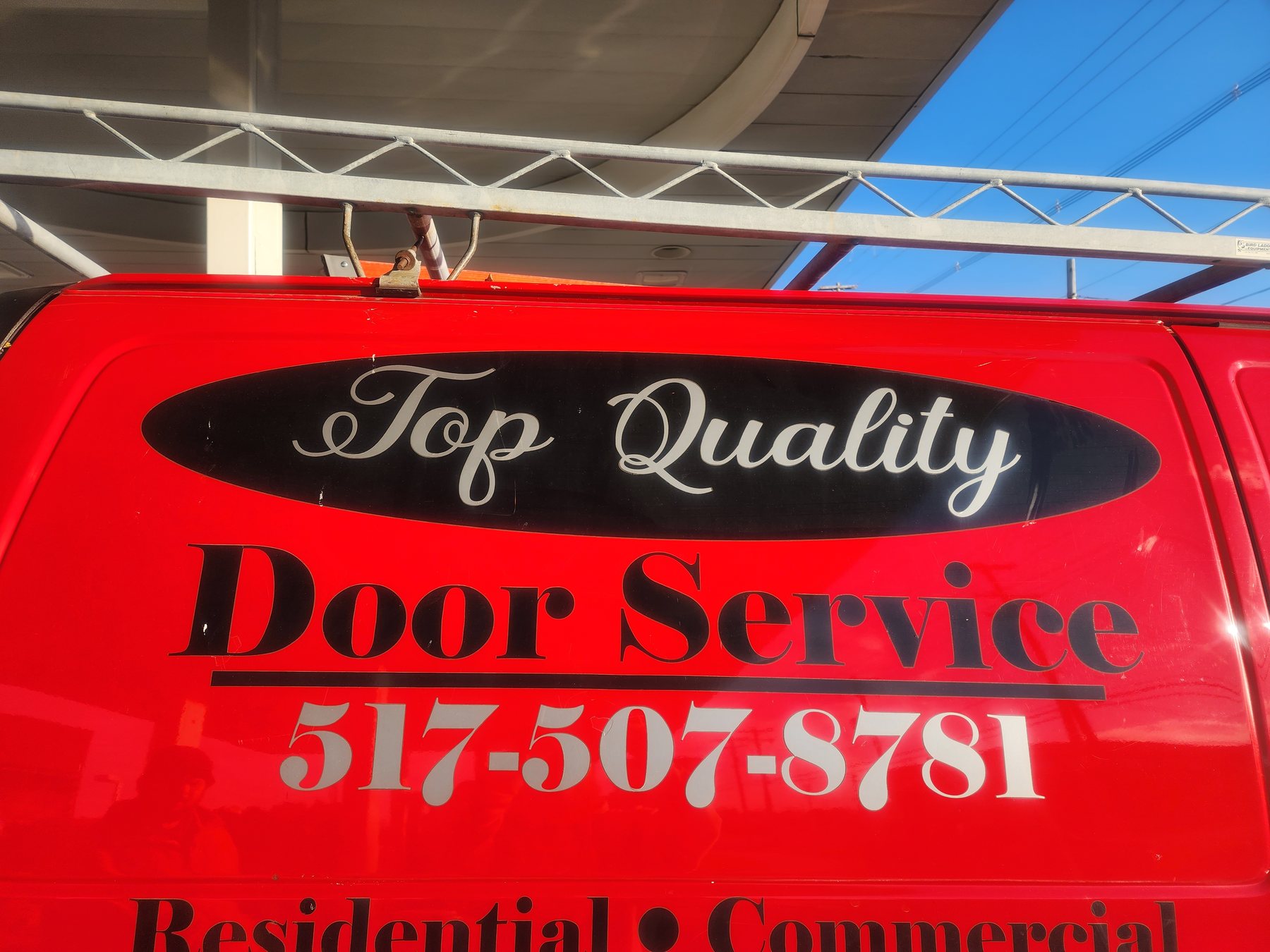 The red Door Service van door with the Top Quality Door Service lettering and phone number